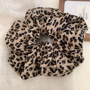 Close-up of leopard print hair scrunchie made of textured fabric on linen background