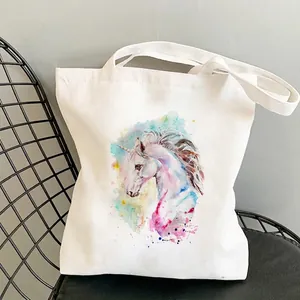 White canvas shoulder bag with colorful watercolor unicorn print on a metal mesh chair