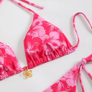 Detail of pink floral bikini top featuring golden flower charm and ruched fabric texture
