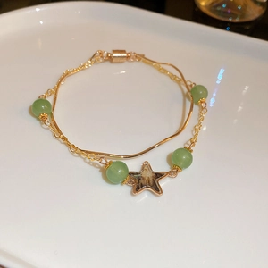 Detailed shot of double-layered gold bracelet with green beads and star pendant decoration