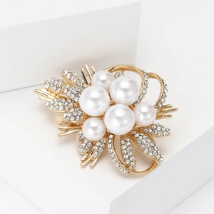 Elegant gold flower brooch featuring white pearls and sparkling rhinestones on a white block