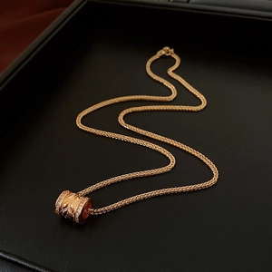 Close-up of a 24k gold plated cylindrical pendant with zircons and woven wheat chain