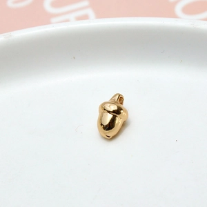 Macro view of a golden acorn-shaped pendant in a white ceramic dish for DIY jewelry making