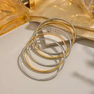 Elegant gold and silver stacked bangle set on silk fabric with a perfume bottle backdrop