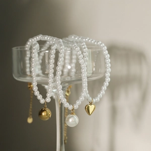Elegant 18K gold plated ball and heart pendant pearl necklaces displayed on a glass