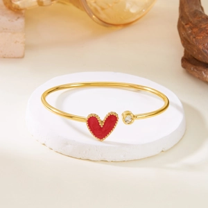 Gold open heart bracelet with red enamel and sparkling zircon on white stone stand