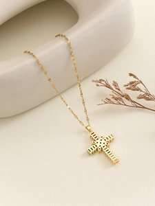 Detail of gold necklace with a colorful zircon cross pendant on white geometric plate