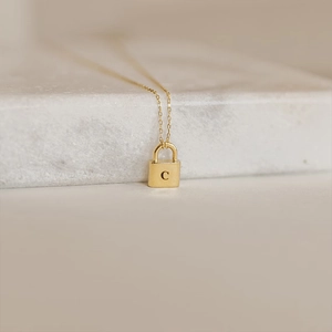 Close-up of golden necklace with a lock-shaped pendant engraved with capital letter C