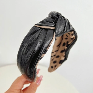 Detail of black faux leather wide headband featuring a top knot and leopard print lining