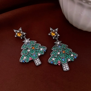 Macro shot of green rhinestone Christmas tree earrings on festive red velvet background