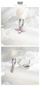 Detailed tile display of asymmetric silver earrings with pink heart wing and fishbone charms