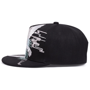 Detail of white crane and cloud embroidery on black cotton snapback baseball cap