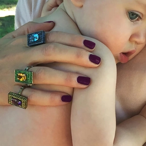 Close-up of a wide square ring with blue gems on a hand holding a baby gently