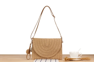 Detail of straw woven crossbody bag featuring semi-circular layered texture and pom poms