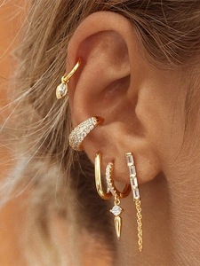 Close-up of golden stud earrings and ear cuffs set with zircon on female ear