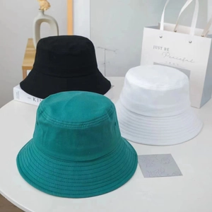 Minimalist cotton bucket hats in black, white and teal on a stylish white desk