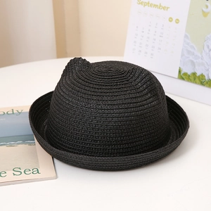 Détail d'un chapeau de paille noir avec oreilles de chat sur un bureau blanc