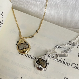 Detailed shot of gold and silver teardrop necklaces with textured stone pendants on a book