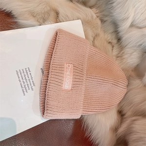 Detail of pink knitted beanie with embroidered THE FOCUS label on soft plush background