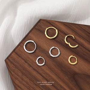 Macro shot of gold and silver S999 silver hoop earrings on walnut wood and silk fabric