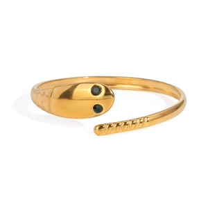Detail of golden snake bangle with green crystal eyes and spiral engraved tail pattern