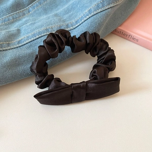 Detail of a black satin silk scrunchie with a bow on a lifestyle background