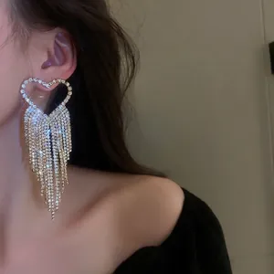 Sparkling oversized heart-shaped rhinestone tassel earrings shown on a female model