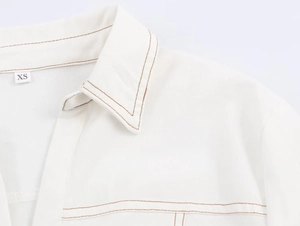 Détail d'une chemise blanche avec surpiqûres marron et étiquette de taille XS au col