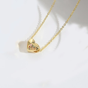 Macro shot of gold heart pendant with colorful enamel patterns and cross chain necklace