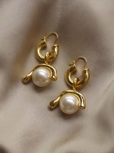 Detailed macro view of retro gold earrings with white pearls on beige silk fabric
