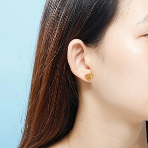 Gros plan de boucles d'oreilles cœur évidé dorées portées sur fond bleu clair