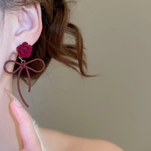 Close-up of elegant red velvet rose earrings with bow pendant on a female model