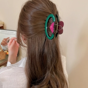 Vue macro d'une pince à cheveux en acrylique verte avec détail de cœur bordeaux sur modèle