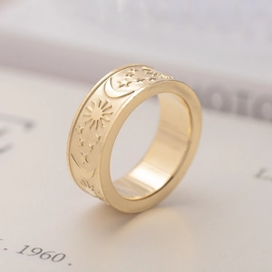 Detalle de primer plano de un anillo de acero dorado con grabados de sol, luna y estrellas.
