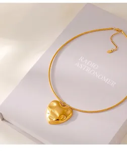 Macro detail of gold hammered heart pendant with a sleek snake chain on a gift box