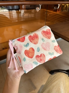 Close-up of small fabric pouch with heart pattern and pink rope handle held in hand