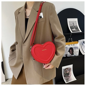 Détail du sac à bandoulière rouge en forme de cœur avec logo doré sur un mannequin