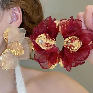 Detail view of large burgundy and champagne fabric flower earrings on a model