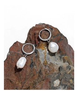 Macro shot of Baroque freshwater pearls on silver hoops against a natural rock texture