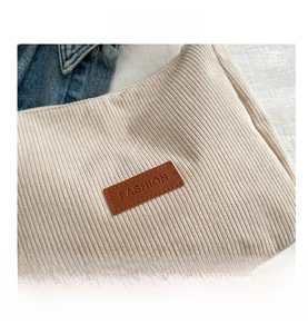 Detailed close-up of corduroy texture and brown leather FASHION label on beige tote bag
