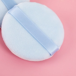 Macro view of light blue soft plush powder puff with satin ribbon on pink background