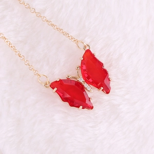 Close-up of golden necklace featuring a vibrant red butterfly pendant with sparkling rhinestones