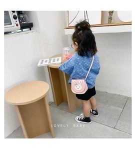 Pink cartoon rabbit crossbody bag for girls styled on a child model in a home setting