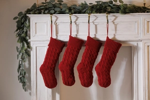 Detail view of four red knitted Christmas stockings hanging on a white mantel with greenery