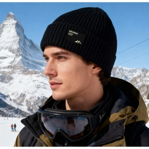 Detail der schwarzen Rippstrickmütze mit Berg-Patch vor einem verschneiten Hintergrund