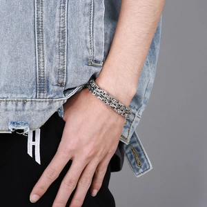 Close-up of a silver men's Byzantine chain bracelet worn by a model in casual denim attire