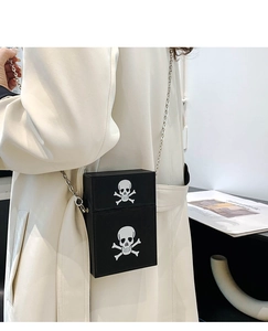 Detail of square skull crossbody bag with silver chain worn over a beige coat