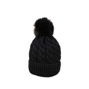Detail of black knit beanie featuring thick cable pattern and large faux fur pom-pom