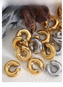 Polished gold and silver C-shaped ear cuffs displayed on natural stone and wood