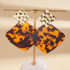 Detailed macro view of geometric square earrings with gold hammered metal and amber resin texture